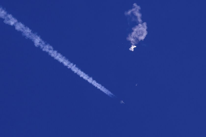 In this photo provided by Chad Fish, the remnants of a large balloon drift above the Atlantic Ocean, just off the coast of South Carolina, with a fighter jet and its contrail seen below it, Saturday, Feb. 4, 2023. The downing of the suspected Chinese spy balloon by a missile from an F-22 fighter jet created a spectacle over one of the state’s tourism hubs and drew crowds reacting with a mixture of bewildered gazing, distress and cheering. (Chad Fish via AP)