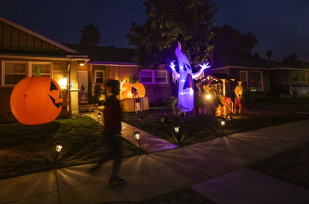 A pedestrian walks past a home illuminated with blow-up jack o'lanterns and a ghost.