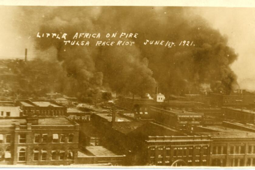 The burning Greenwood District during the Tulsa Race Massacre, 1921. First Street is visible in the foreground on which is located the Bessemer Gas Engine Company and the Eagle Hotel. The back of the photograph contains a notation stating, "Building in foreground with arched front - Tulsa Opera House on 2nd between Boston and Cincinnati. 113 E. 2nd St."