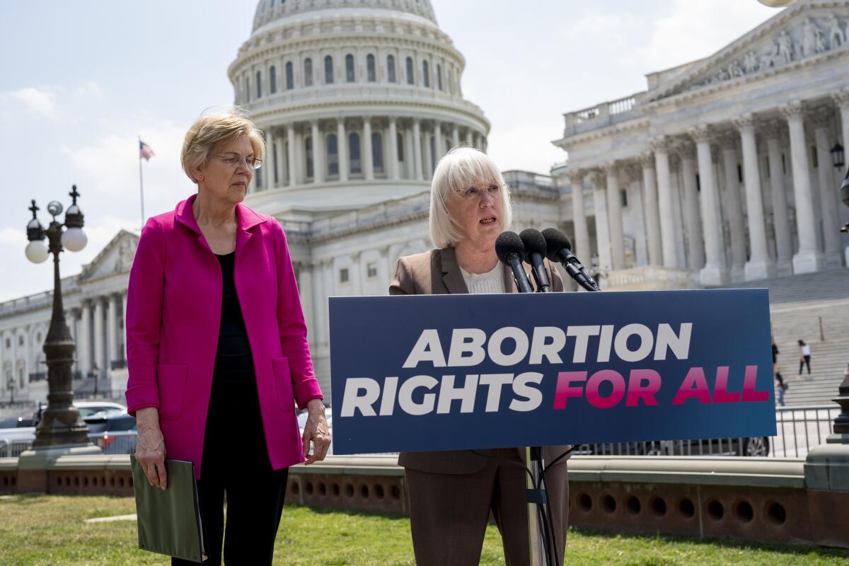 Sen. Patty Murray speaks behind a sign that says "Abortion rights for all." Sen. Elizabeth Warren is beside her.