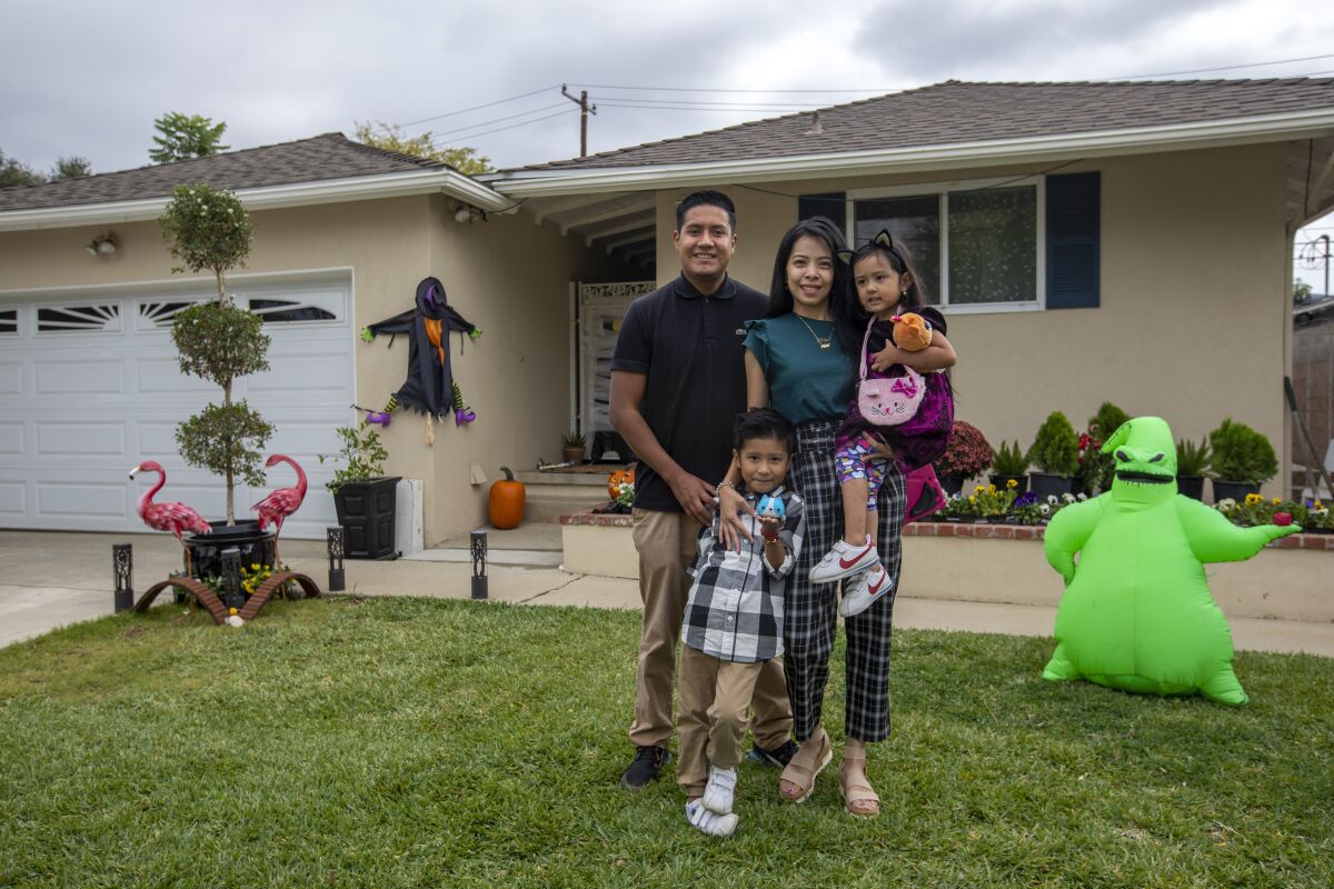 A man and woman and two children stand in front of a home decorated for Halloween.
