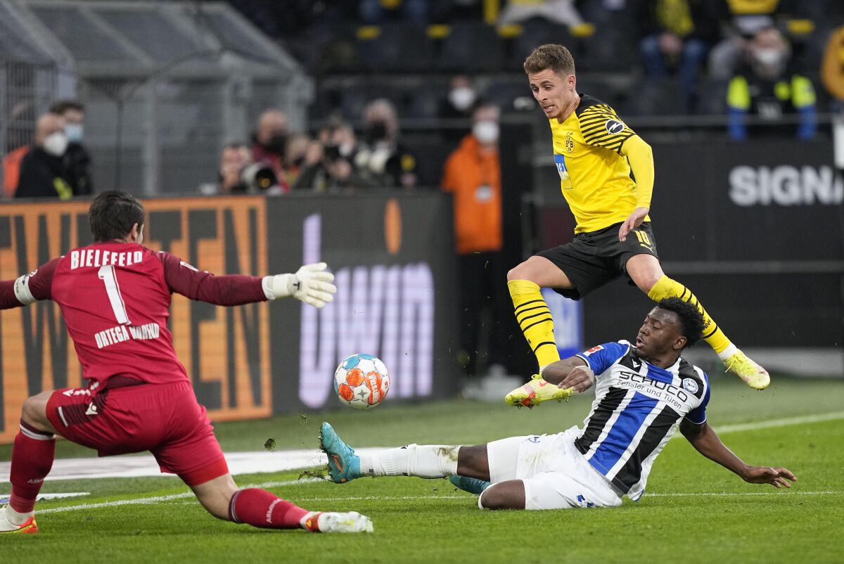 Dortmund's Thorgan Hazard, up, and Arminia's George Bello challenge for the ball in front of Arminia's goalkeeper Stefan Ortega, left, during the German Bundesliga soccer match between Borussia Dortmund and Arminia Bielefeld in Dortmund, Germany, Sunday, March 13, 2022. (AP Photo/Martin Meissner)