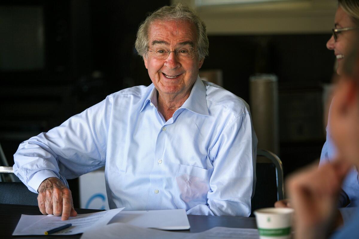 Wine industry pioneer Warren Winiarski in a blue button-up shirt smiling while sitting at a table.
