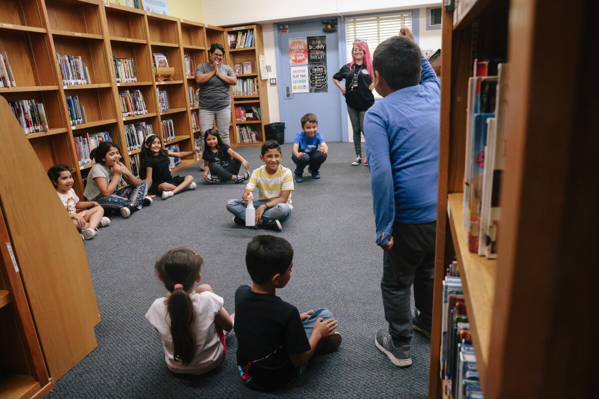 Young students sit on the carpet inside a school library. 