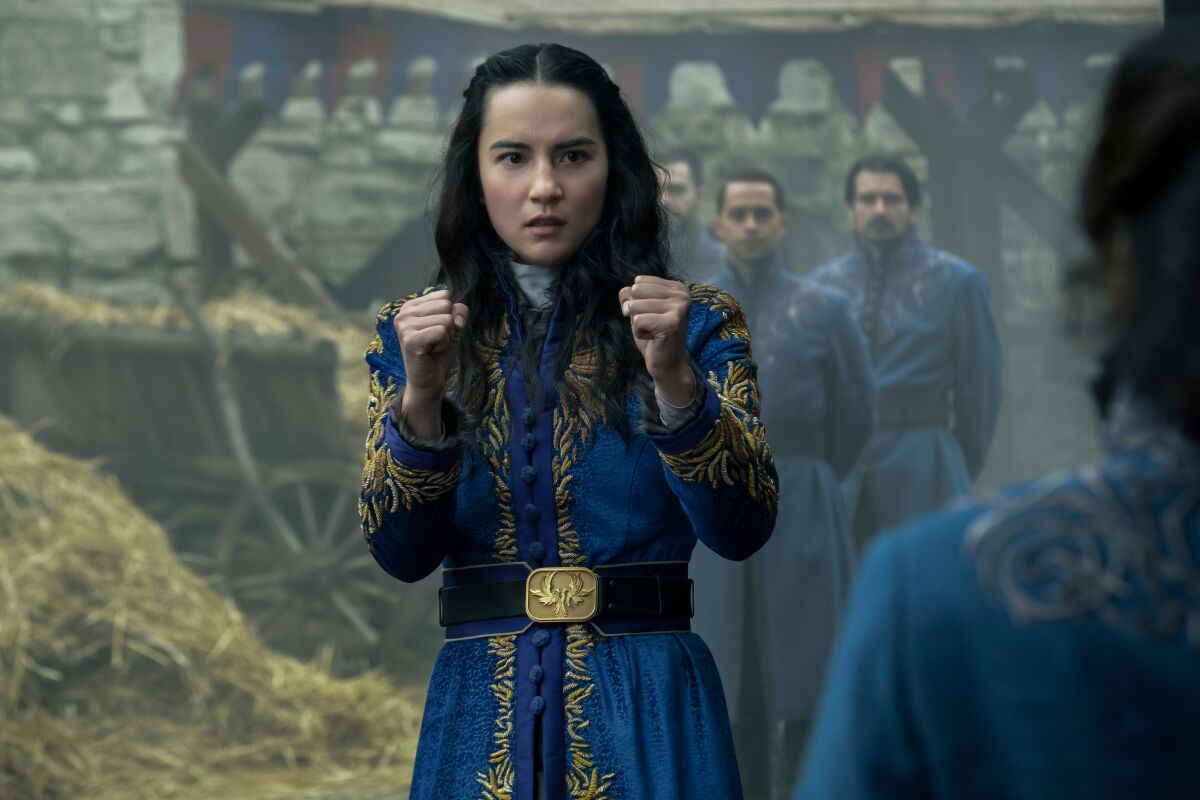 A young woman in a blue and gold dress puts her fists up prepared to fight