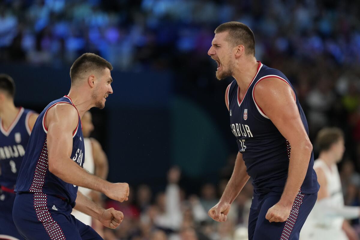 Nikola Jokic yells and balls his hands into fists at his sides with a teammate nearby