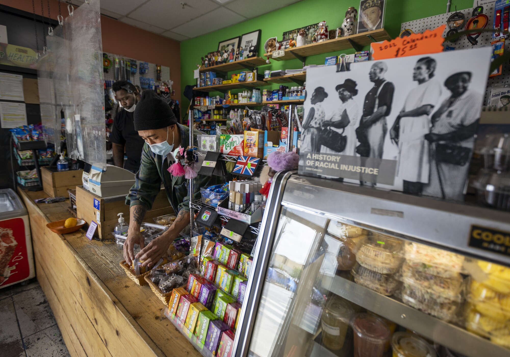 mployee Mark Burton, left, works the cash register as Danny Park, owner and market director, stocks the counter baskets
