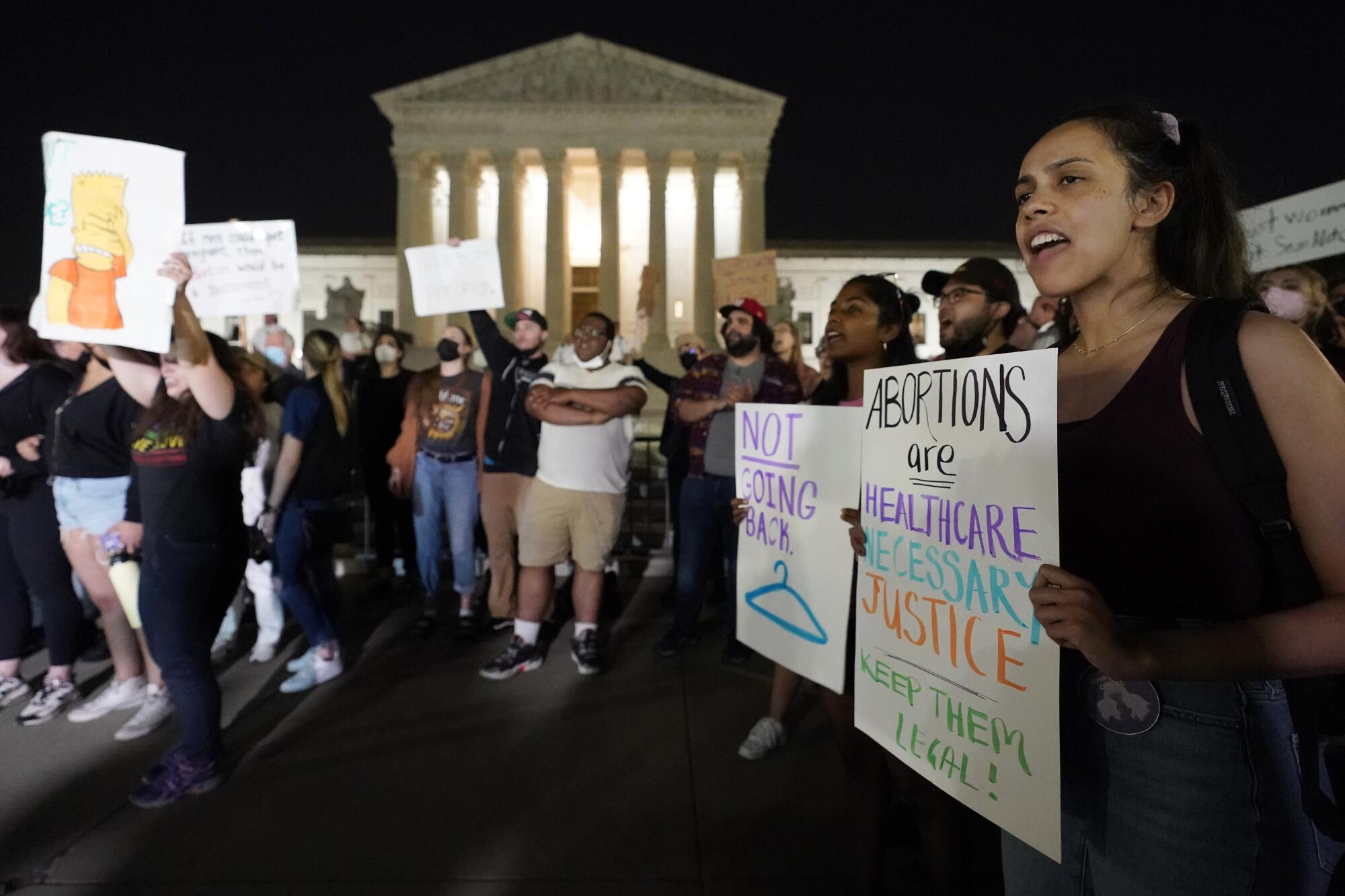 Protesters hold signs reading "Not Going Back" with a picture of a coat hanger, and "Abortions Are Healthcare."