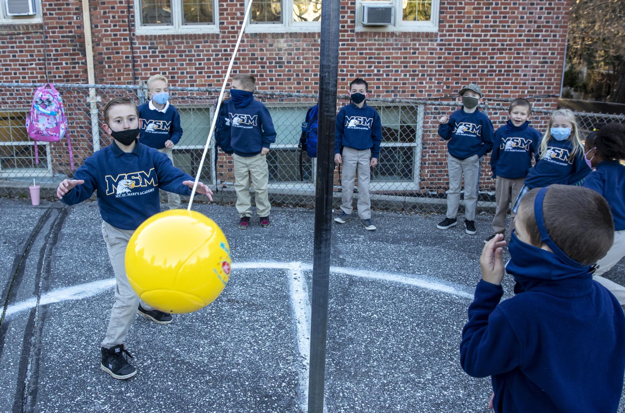 Two children in masks play tetherball as other students line up to watch