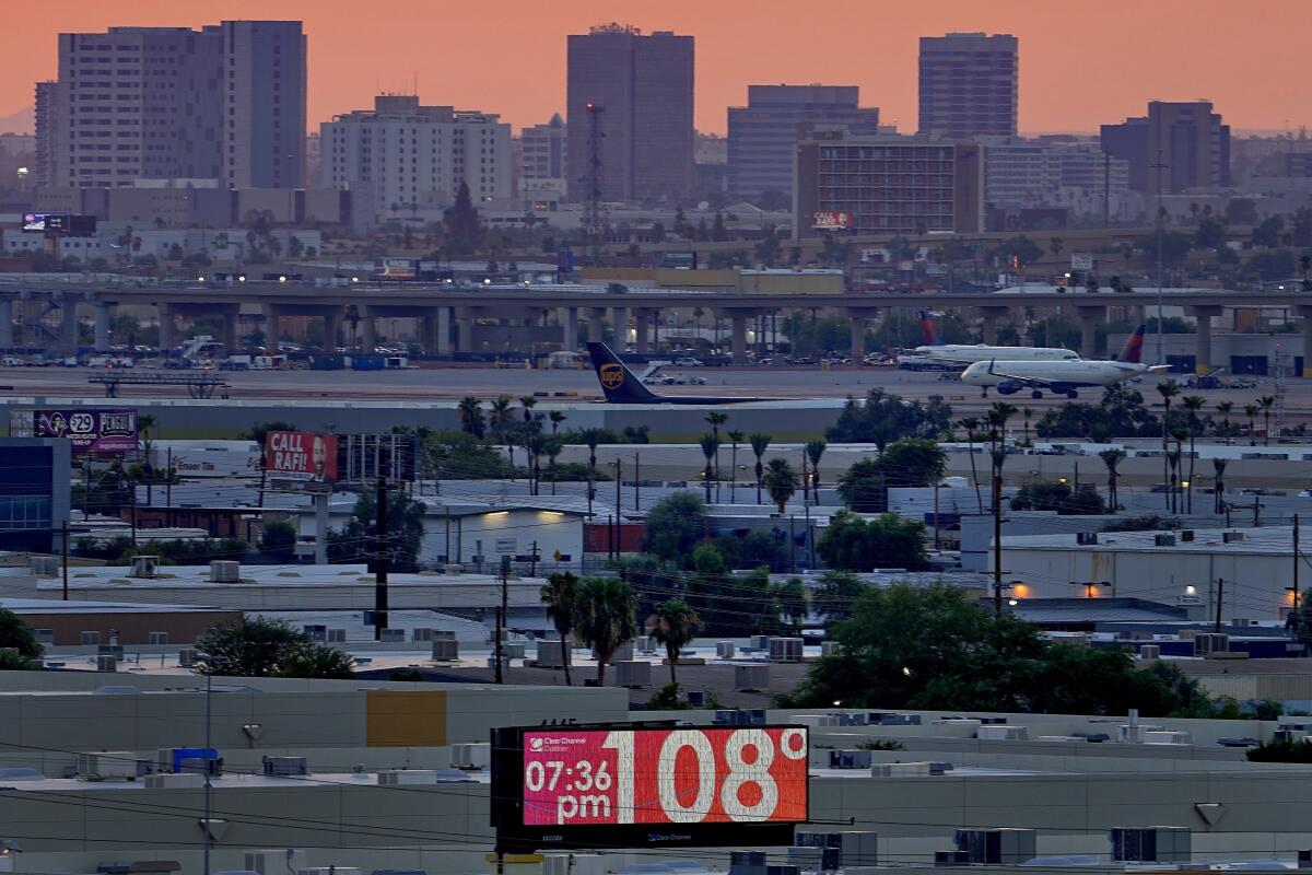 A sign displays a temperature of 108 with airplanes, buildings and orange skies as the backdrop