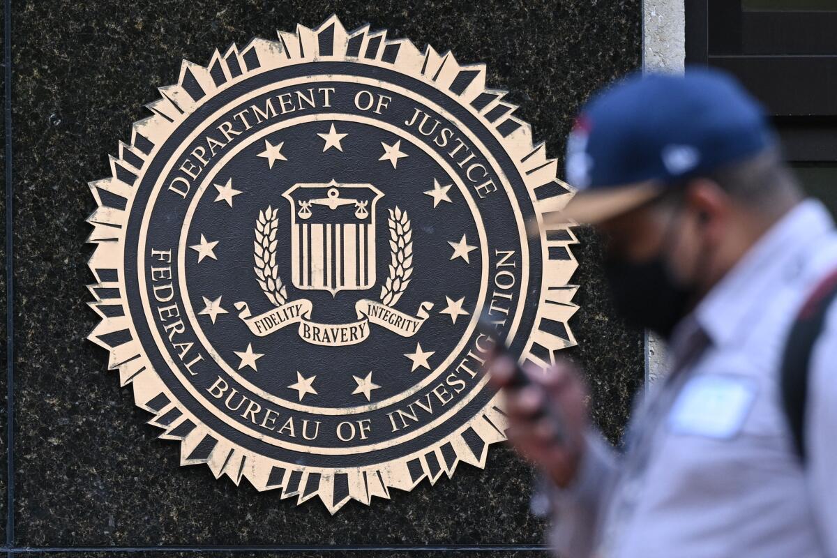 A pedestrian walks past a seal reading Department of Justice Federal Bureau of Investigation..