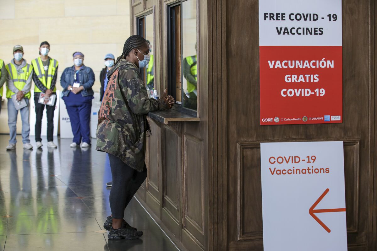 A woman in a mask stands at a counter near a sign that says "Free COVID-19 vaccines."