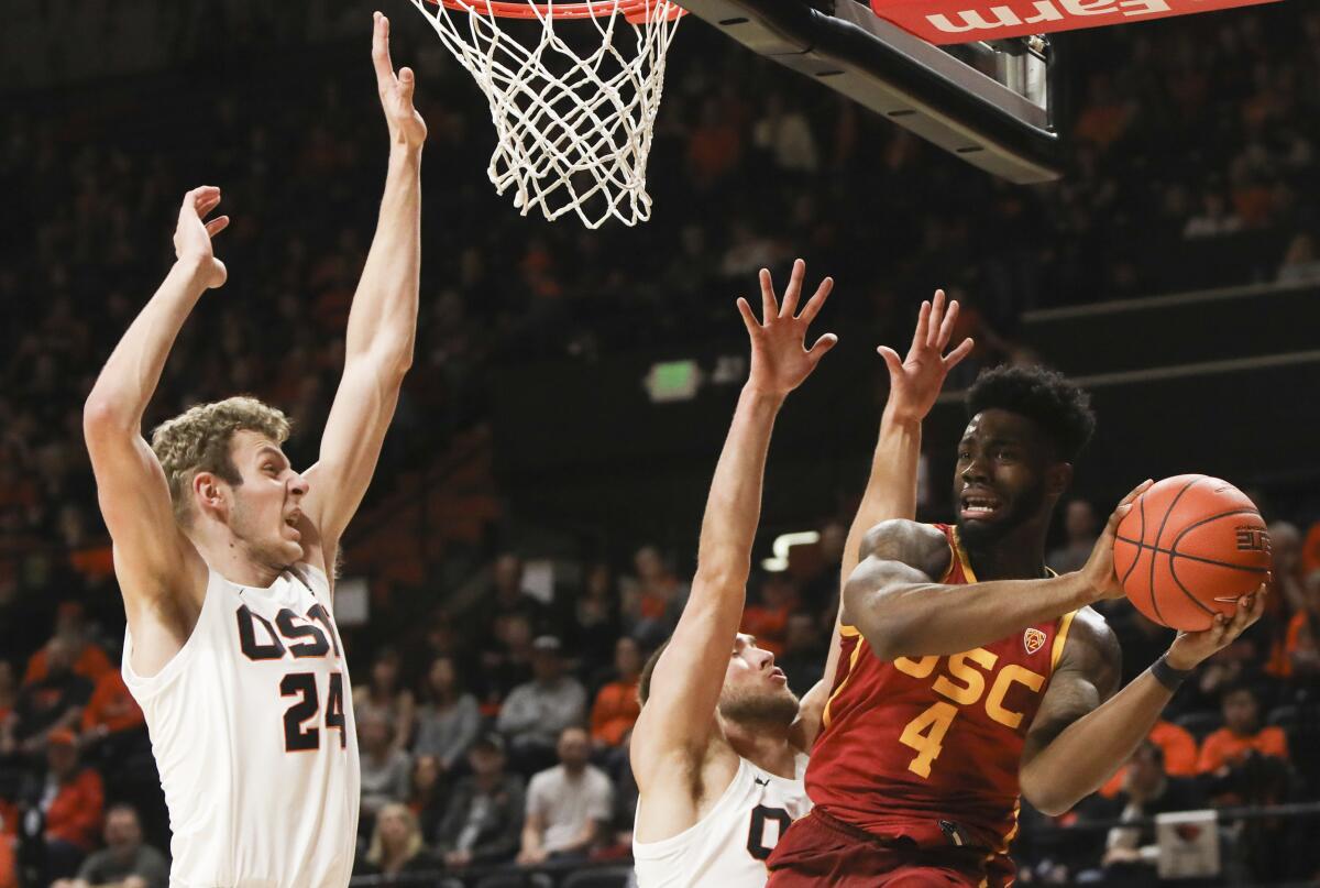 USC's Daniel Utomi (4) passes away from the basket to avoid Oregon State's Kylor Kelley (24) and Tres Tinkle (3) during the first half on Saturday.