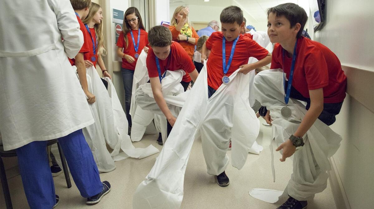 Sixth-graders dress in surgical suits and caps before entering a lab at the Jeffrey M. Carlton Heart & Vascular Institute at Hoag Hospital in Newport Beach to try out robotic technology.