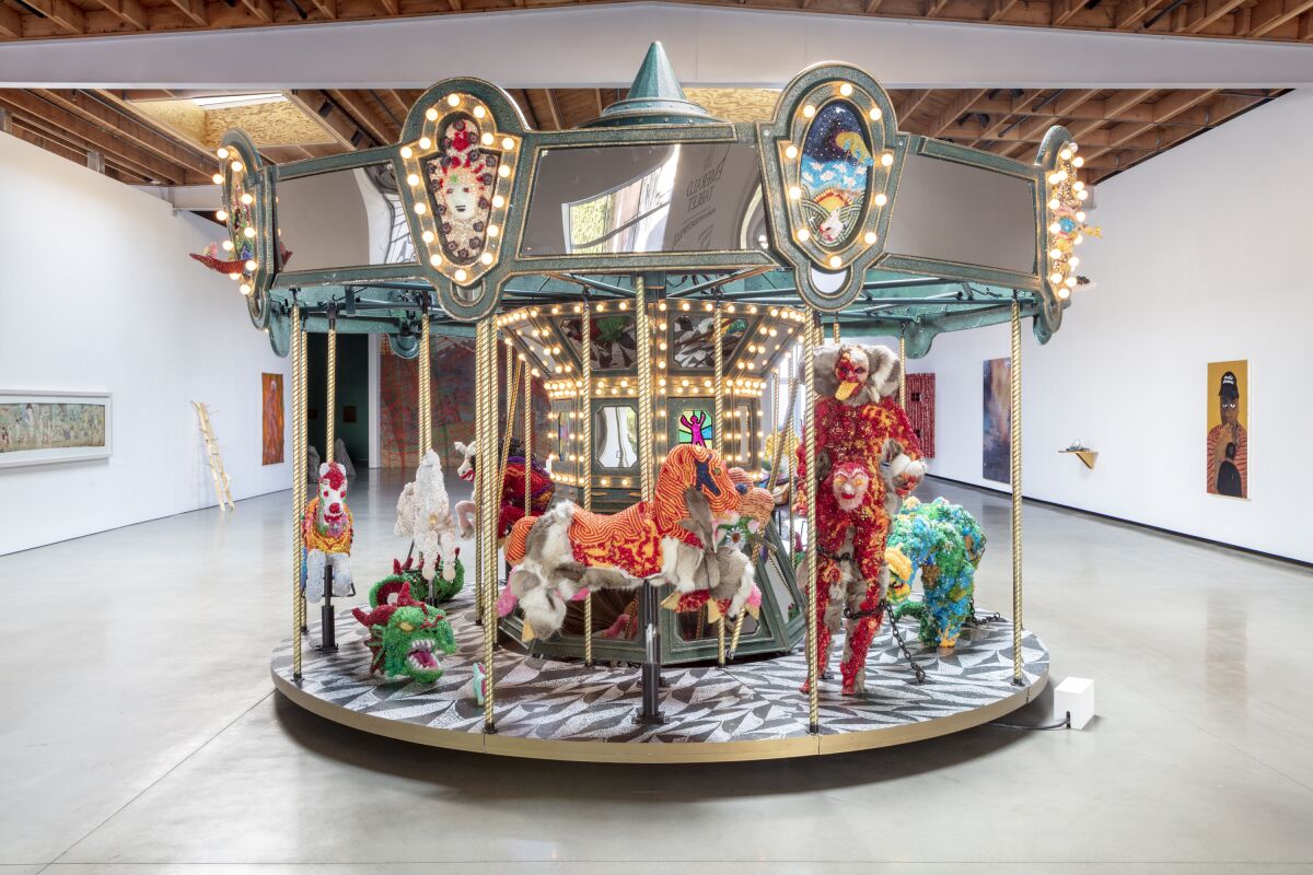 A working carousel inside a gallery space features monstrous and fantastical figures covered in beads and glass.