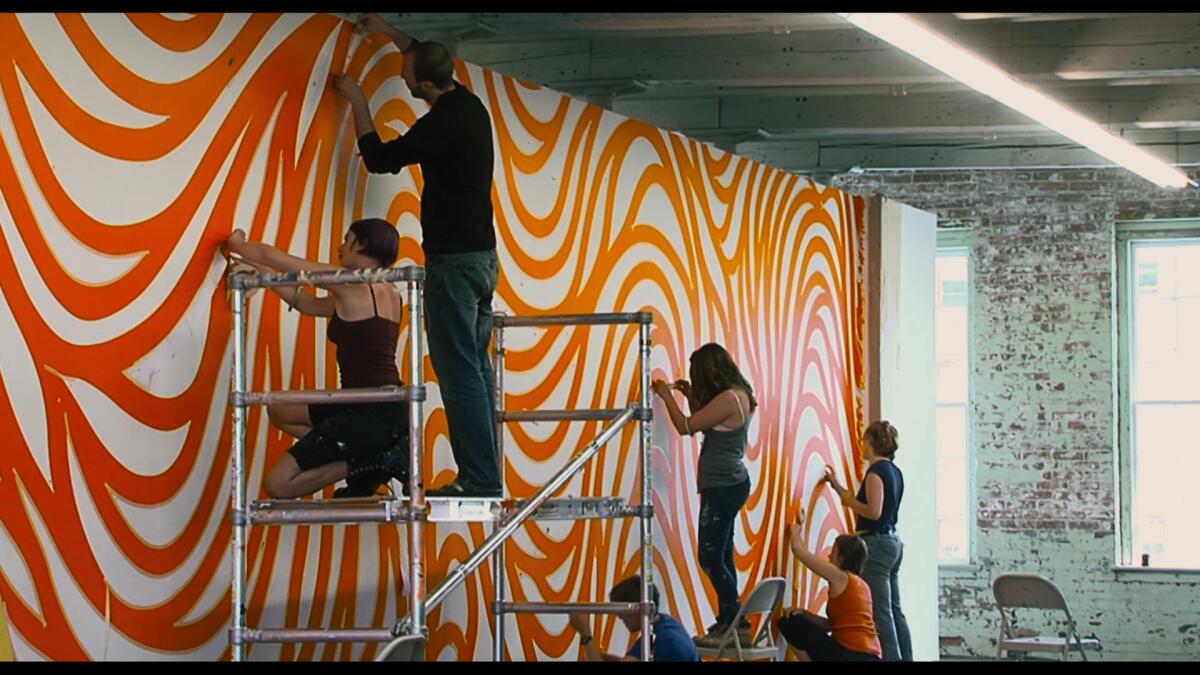 Installers use painted to produce a swirling orange pattern on a museum wall