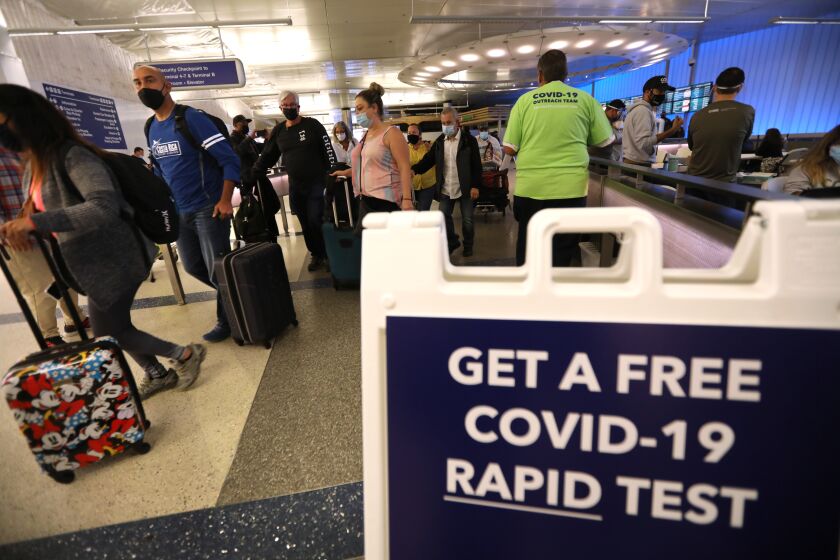 LOS ANGELES, CA - DECEMBER 3, 2021 - Arriving travelers walk past a sign directing them to get a free COVID-19 Rapid Test at the Tom Bradley International Terminal at Los Angeles International Airport Friday, December 3, 2021. In partnership with the state and U.S. Centers for Disease Control and Prevention, the county set up a free rapid testing site for arriving passengers. They were also gave those testing negative a kit they can use to test themselves again three to five days later, in line with CDC recommendations for international travelers coming to the U.S., regardless of vaccination status. Dr. Barbara Ferrer, director of L.A. County Department of Health, was on hand trying to direct arriving passengers to take a free COVID-19 test. (Genaro Molina / Los Angeles Times)