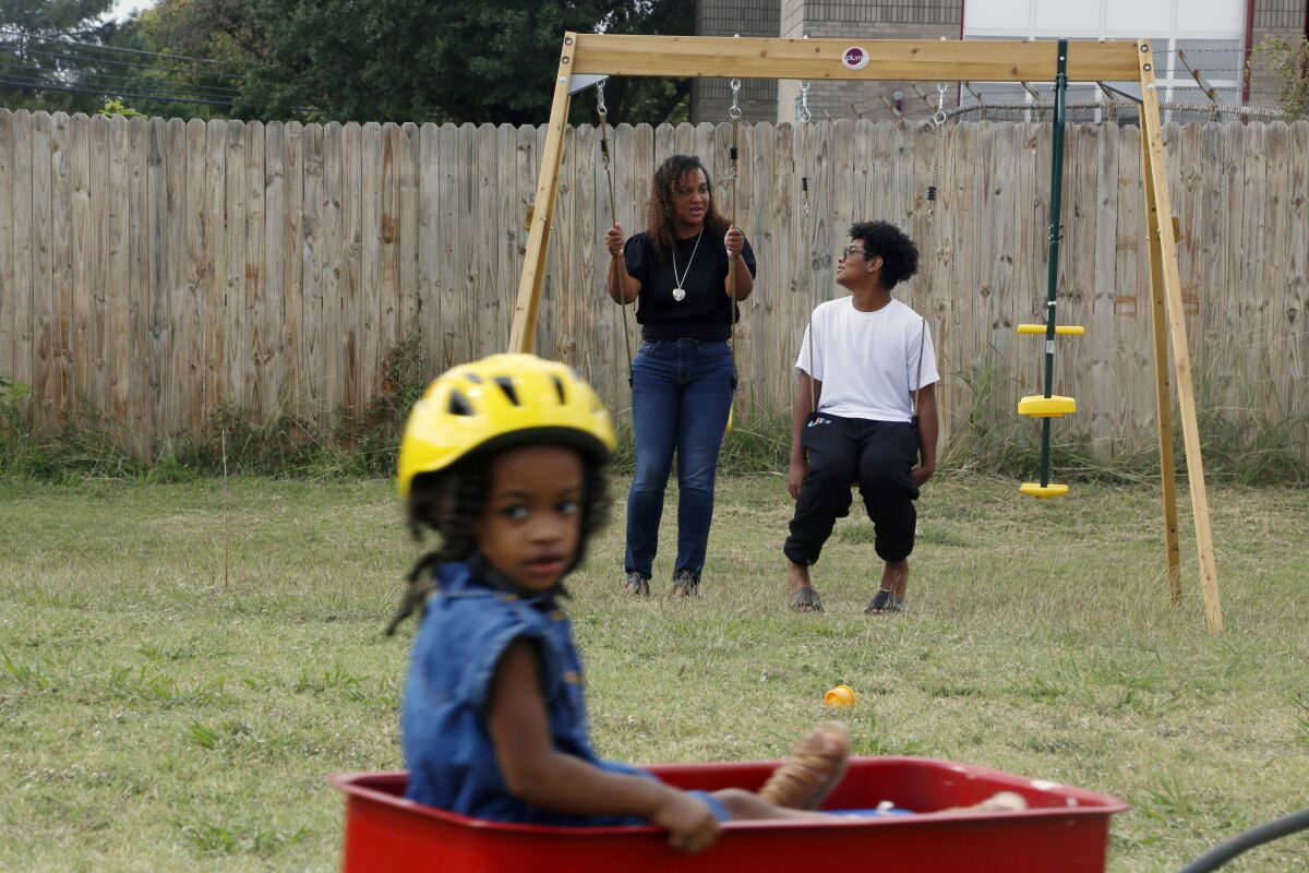 FILE - Rosalia Tejeda, talks with her 13-year-old son, Juscianni Blackeller, while her 2-year-old daughter, Audrey Gray, rides in a wagon in their backyard in Arlington, Texas, on Sunday, Oct. 24, 2021. As Tejeda has learned more about health risks posed by fracking for natural gas, she has become a vocal opponent of a plan to add more natural gas wells at a site near her home. On Tuesday, Jan. 4, 2022, the Arlington City Council voted 5-4 to reject the request by Total Energies to drill additional gas wells, reversing a preliminary decision by the council in November to allow the wells to go forward. (AP Photo/Martha Irvine)