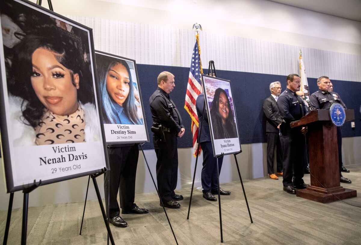 Photos of three young women stand on display while a group of police officers stands nearby.