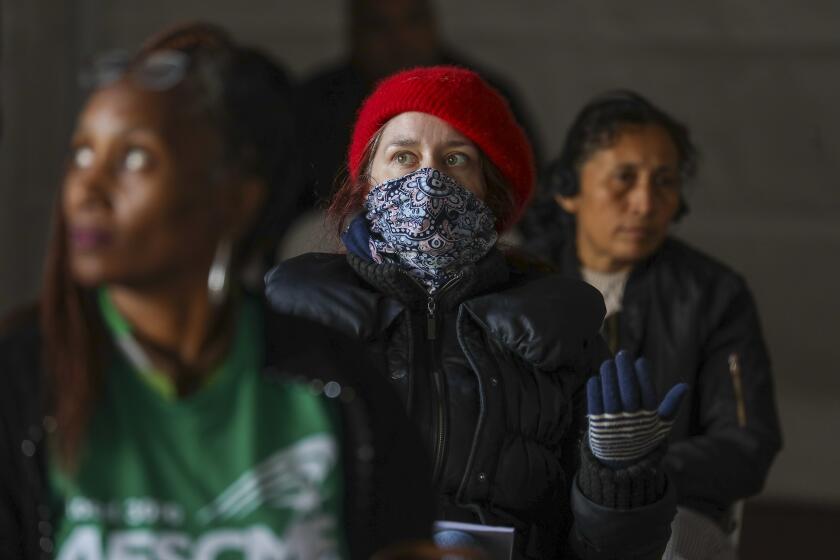 LOS ANGELES, CA - MARCH 17, 2020 - Rachel Carlson, center, and others watch Los Angeles City Council meeting sitting under a tent erected outside city hall amid the threats of the novel coronavirus. A television live streamed video of meeting and public offered comments electronically. (Irfan Khan / Los Angeles Times)