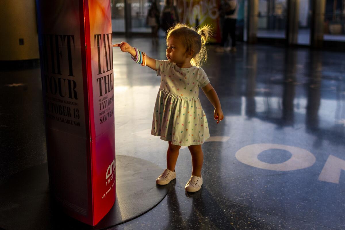 Zealand Birnbaum, 1, of West Hollywood points to a Taylor Swift poster before attending the Taylor Swift concert movie with her mom at the AMC theater on October 13, 2023 in Century City, California.