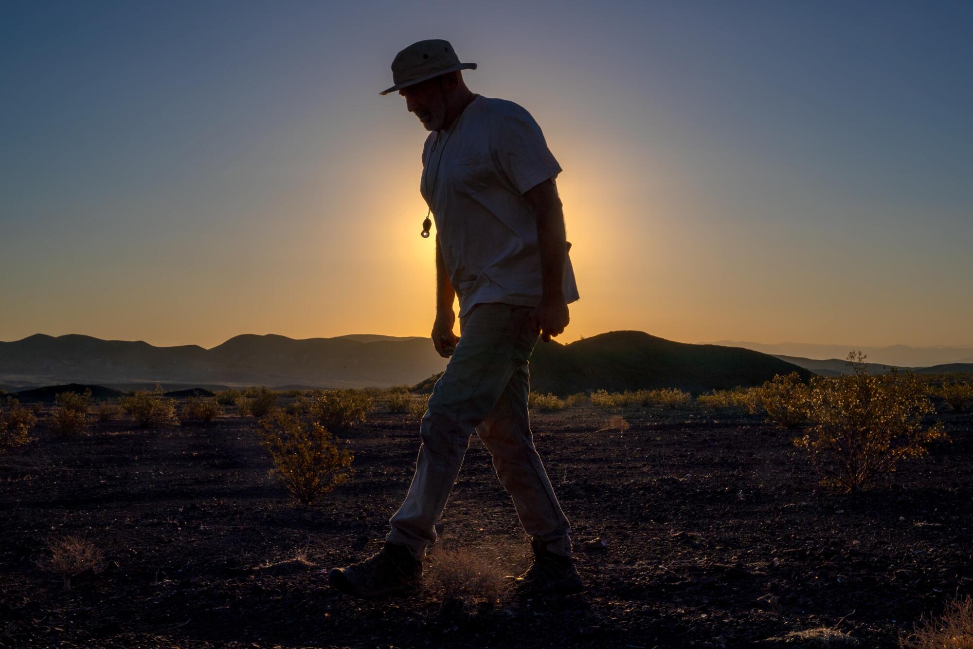 A man's figure is silhouetted by the rising sun as he strides through the desert.