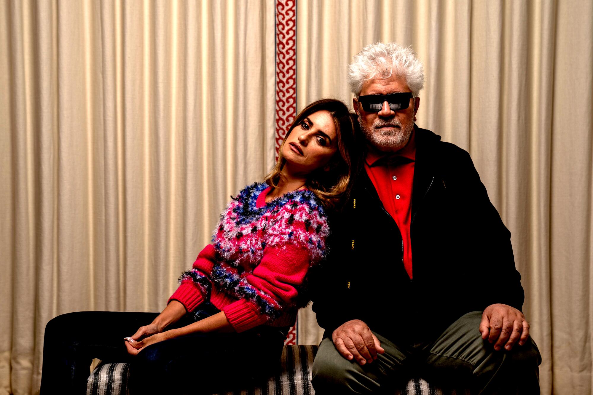 A woman in a red winter sweater leans against a man with spiky white hair and sunglasses 