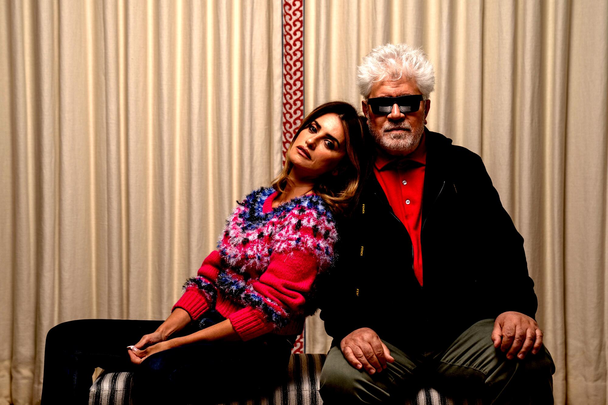 A woman in a red winter sweater leans against a man with spiky white hair and sunglasses