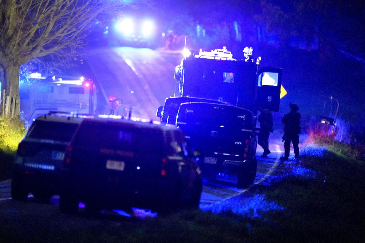 Law enforcement officers stand near armored and tactical vehicles at night.