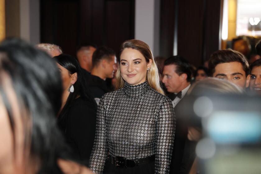 A young woman in a black-and-silver turtleneck stands amid a crowd at an awards show