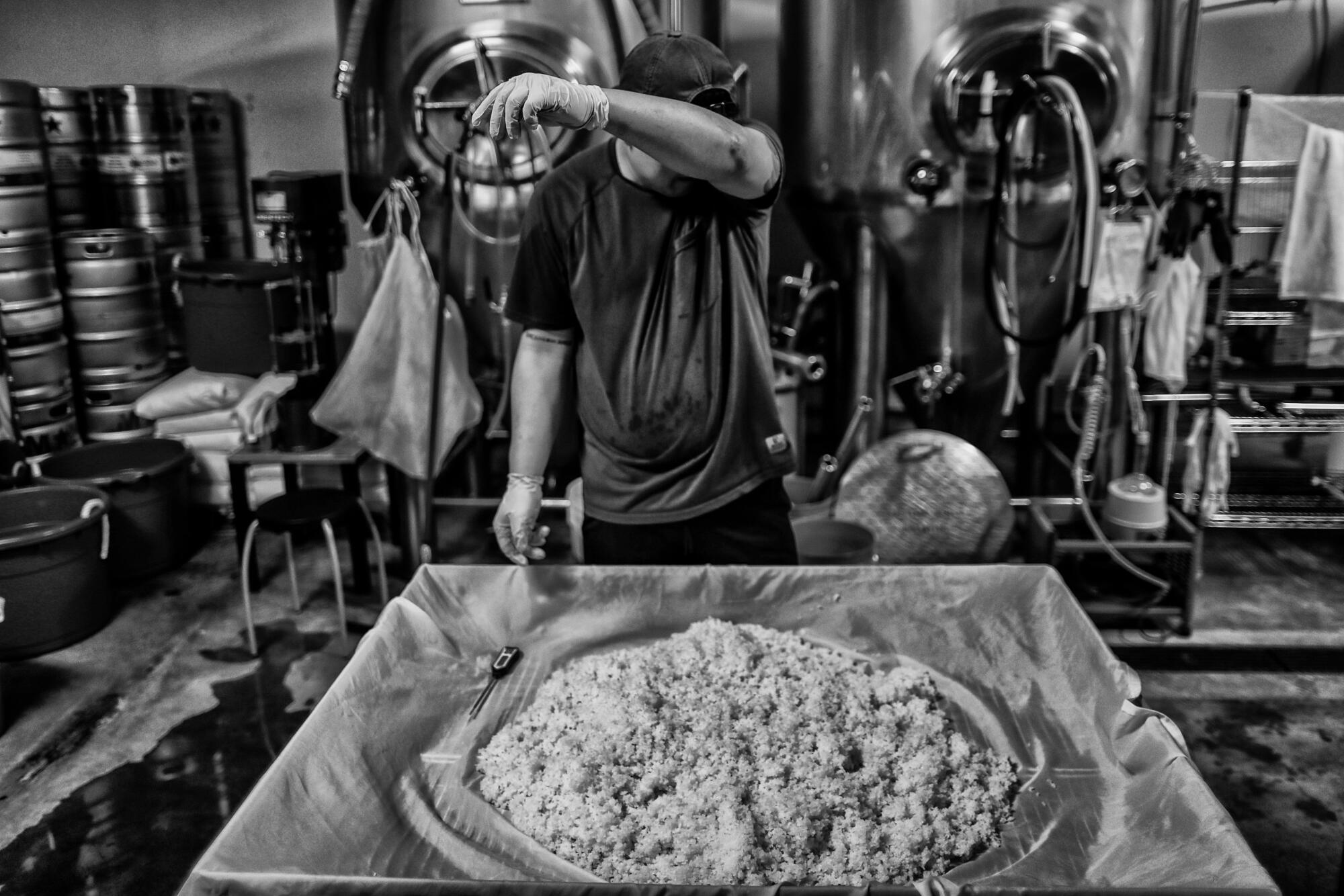 A worker wipes his brow as he stands before a pile of rice 