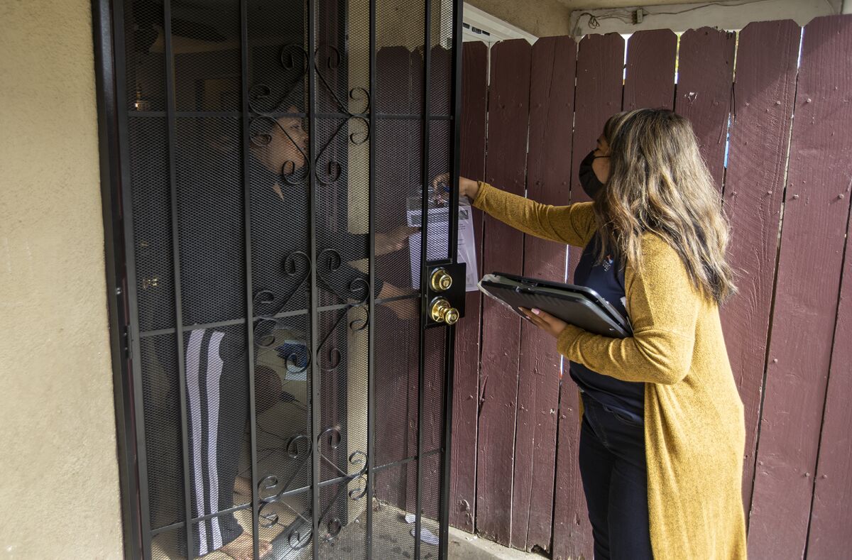 A woman hands fliers through the front door to a resident