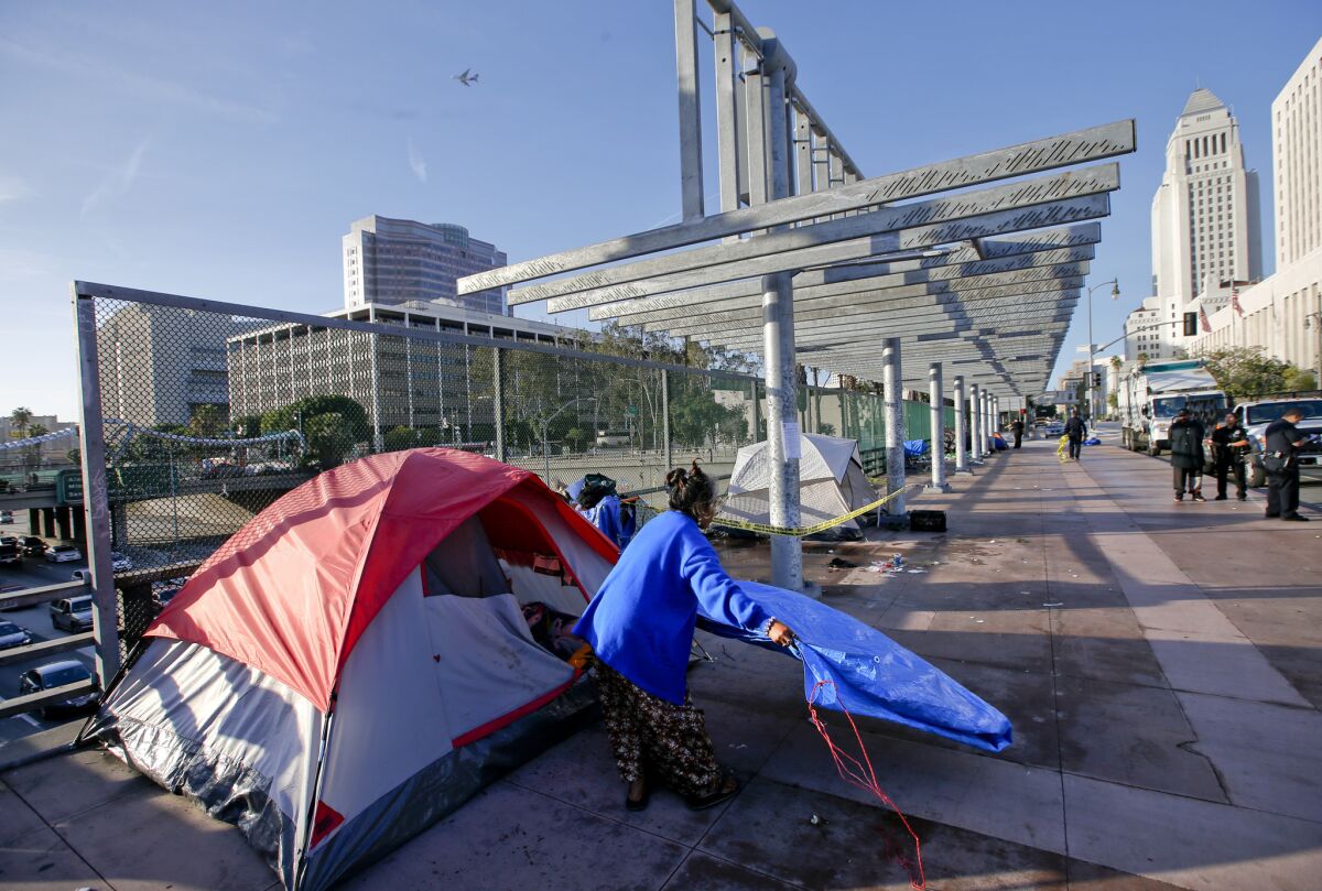 Ry Thounry, 50, takes down her tent on the Main Street overpass above the 101 Freeway in downtown Los Angeles while sanitation crews move in to clean the area.