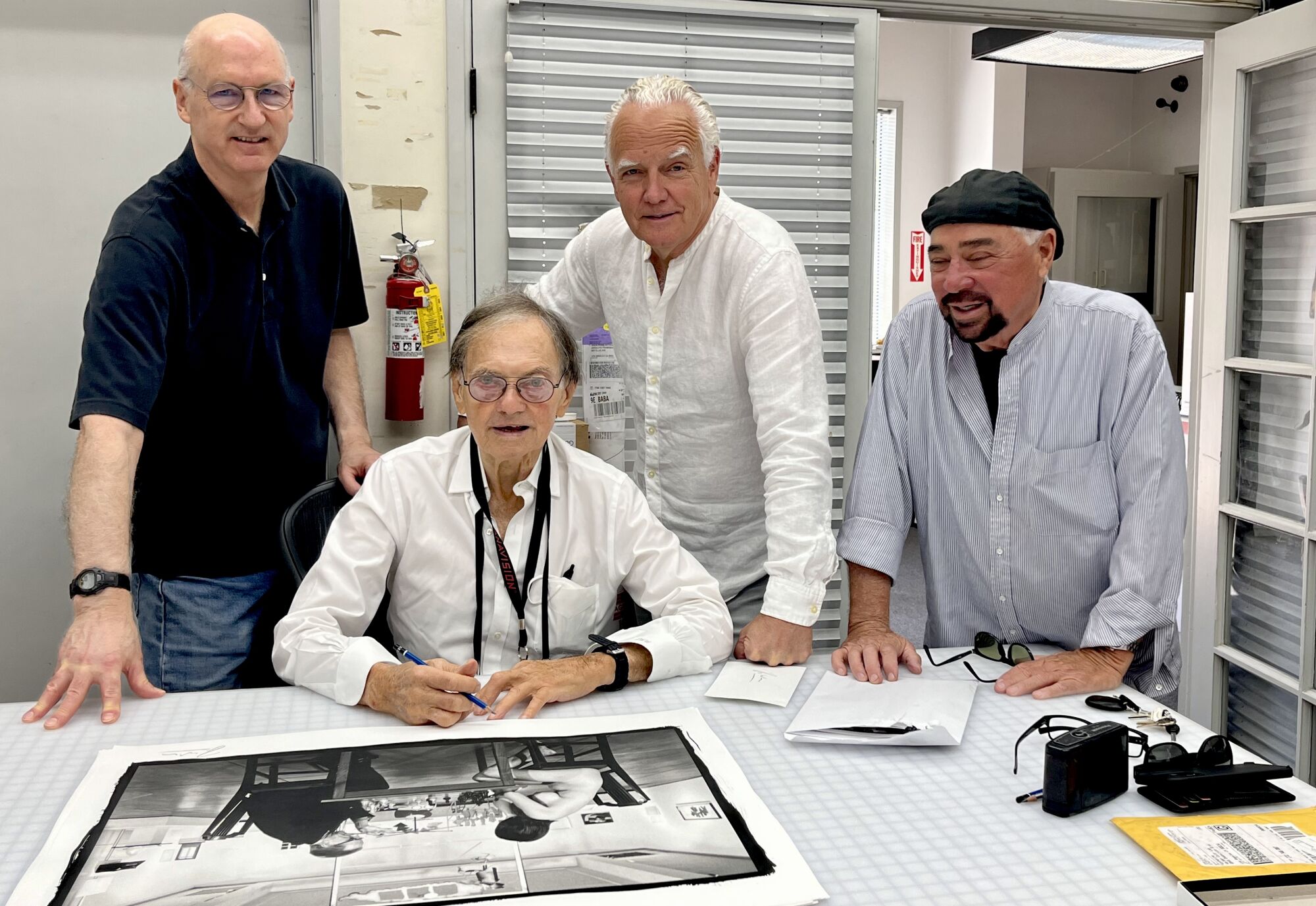 Julian Wasser in 2022, seated, signing a print of his famous photo of Marcel Duchamp and a nude Eve Babitz playing chess.