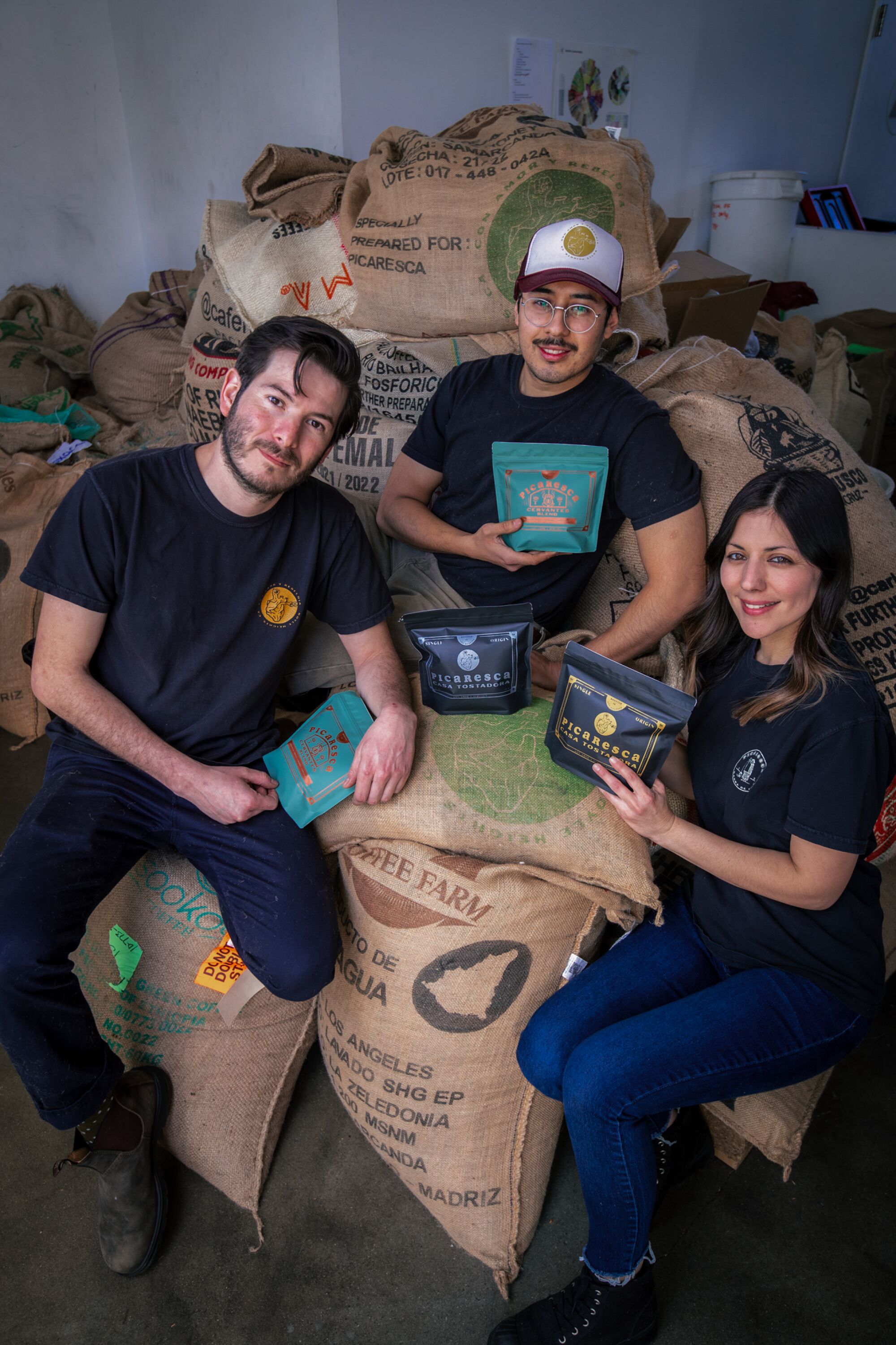 Two men and a woman sit on a pile of burlap sacks full of coffee