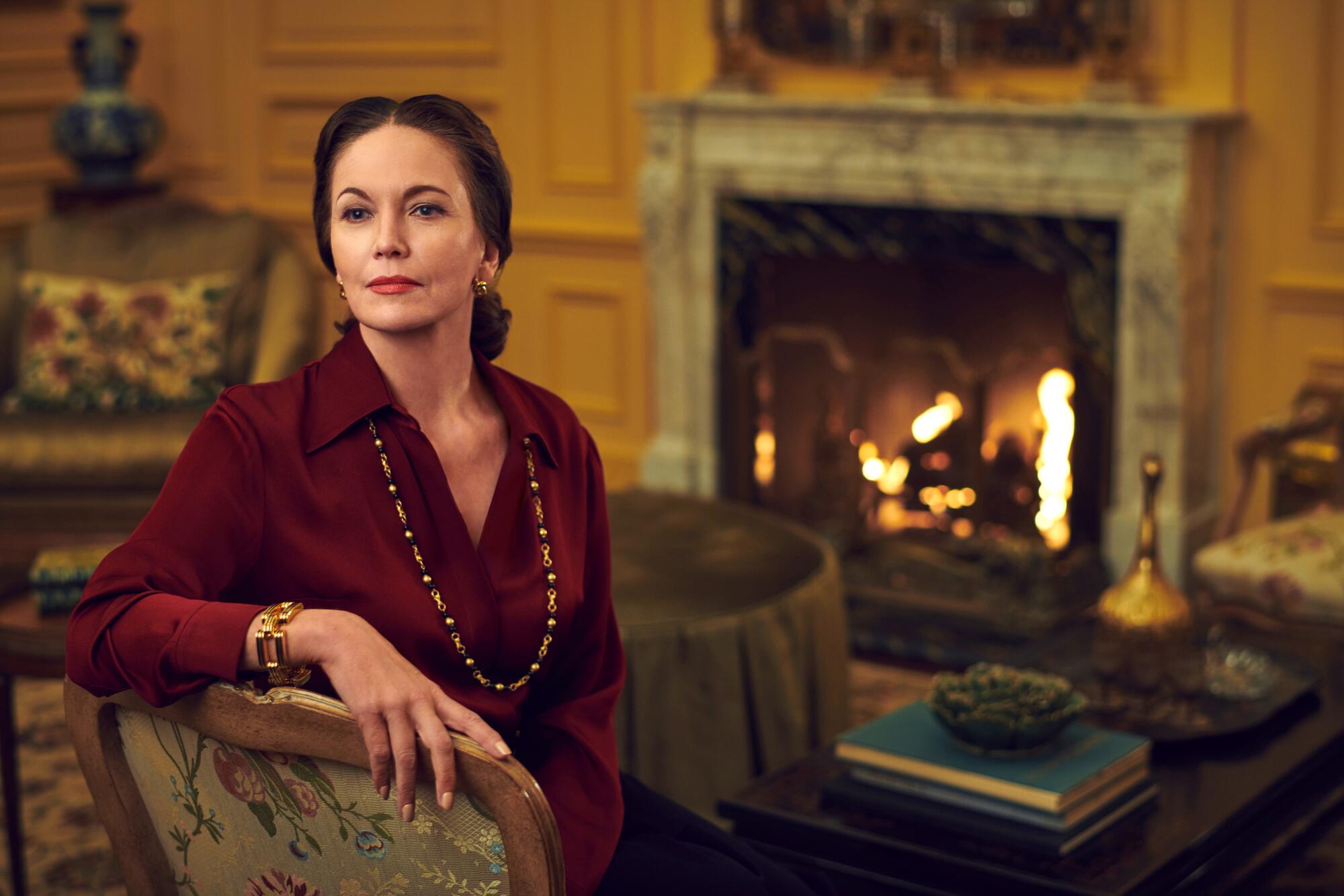 Diane Lane as Slim Keith sits perfectly straight in a chair in front of a fire for "Feud."