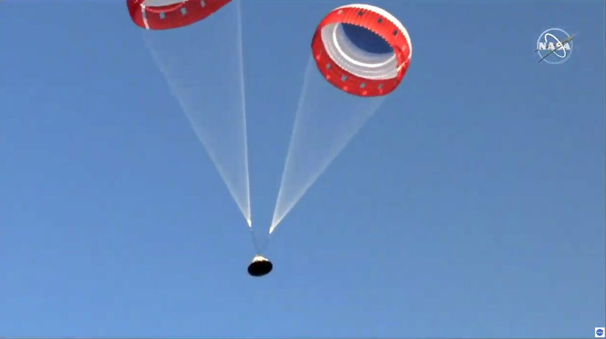 Orange nd white parachutes guide Boeing's Starliner capsule in the blue sky