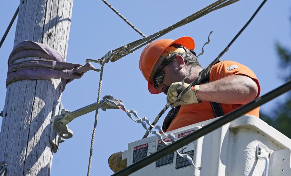 FILE - In this Wednesday, Aug. 4, 2021, file photo, Travis Sheetz, a worker with the Mason County (Wash.) Public Utility District, installs fiber optic cable on a utility pole, while working with a team to bring broadband internet service to homes in a rural area surrounding Lake Christine near Belfair, Wash. (AP Photo/Ted S. Warren, File)