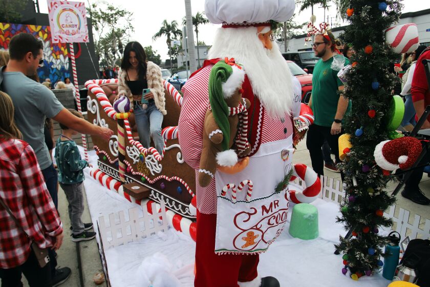 Guests have their picture taken as they sit in a big candy sleigh at B. Candy during the annual Corona del Mar Christmas Walk in the Corona del Mar Village along Pacific Coast Highway on Sunday, December 4, 2022. The Christmas walk is a holiday celebration with live entertainment, visits from Santa, beer and wine, vendor gifts and children activities. (Photo by James Carbone)