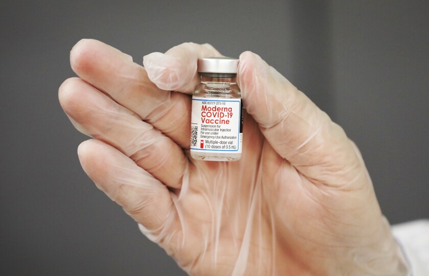 Closeup of a gloved hand holding a vial of vaccine.