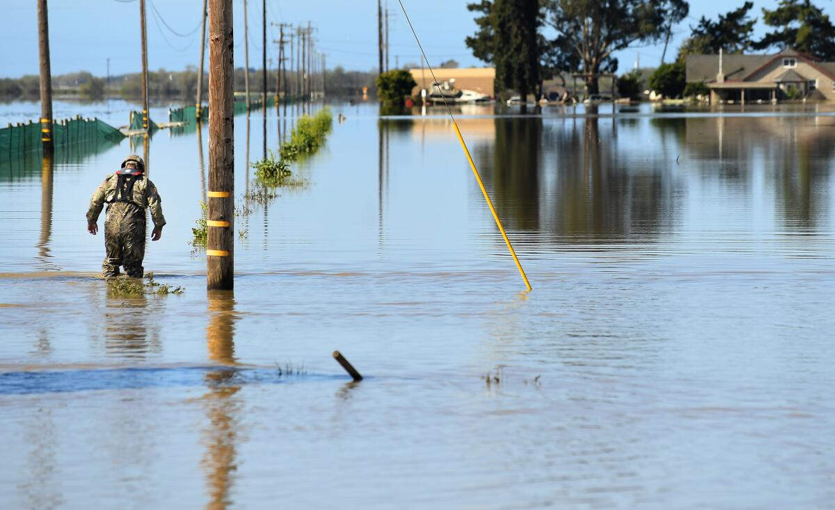 A uniformed guardsman wades through knee-high water near homes, power lines and fields.
