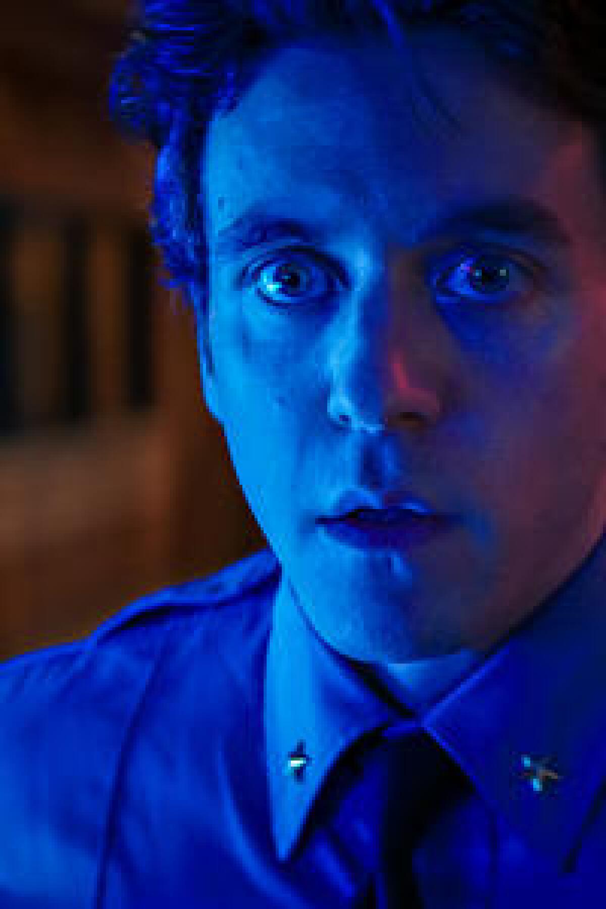 An officer in uniform with wide eyes, bathed in blue light.