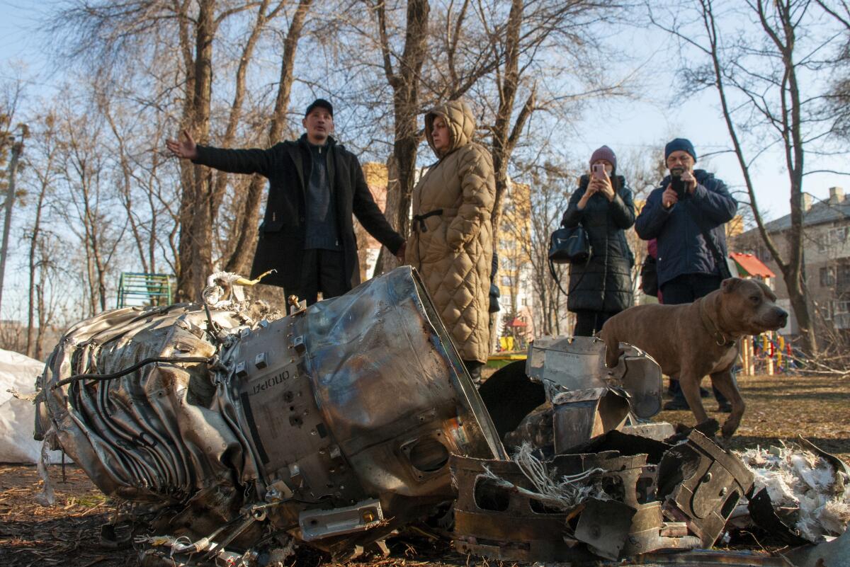 Gente de pie ante fragmentos de equipamiento militar en una calle tras un aparente ataque ruso en Járkiv, Ucrania.