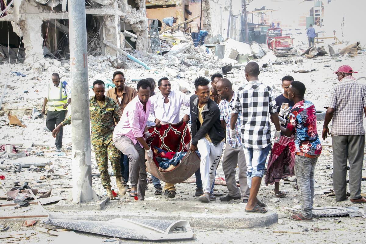 People carry an injured person  through rubble after a bombing.
