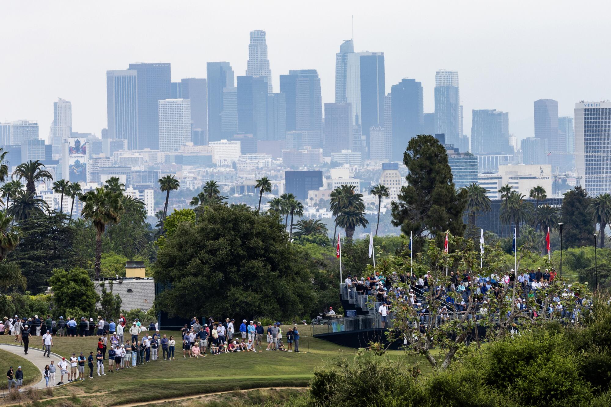 People gather in a lush park with the Los Angeles city skyline in the background. 