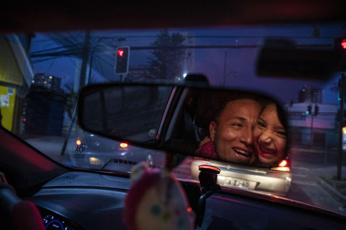 Reflected in the rearview mirror, Jose Collantes gets a hug from daughter Kehity while they're stopped at a red light, as Jose drives his five-year-old home from a playdate in Santiago, Chile, Sunday, Sept. 6, 2020, three months after they lost his wife, her mother, to COVID-19. Their case highlights how COVID-19 deaths the world over are often the beginning of a new personal journey for those affected. (AP Photo/Esteban Felix)
