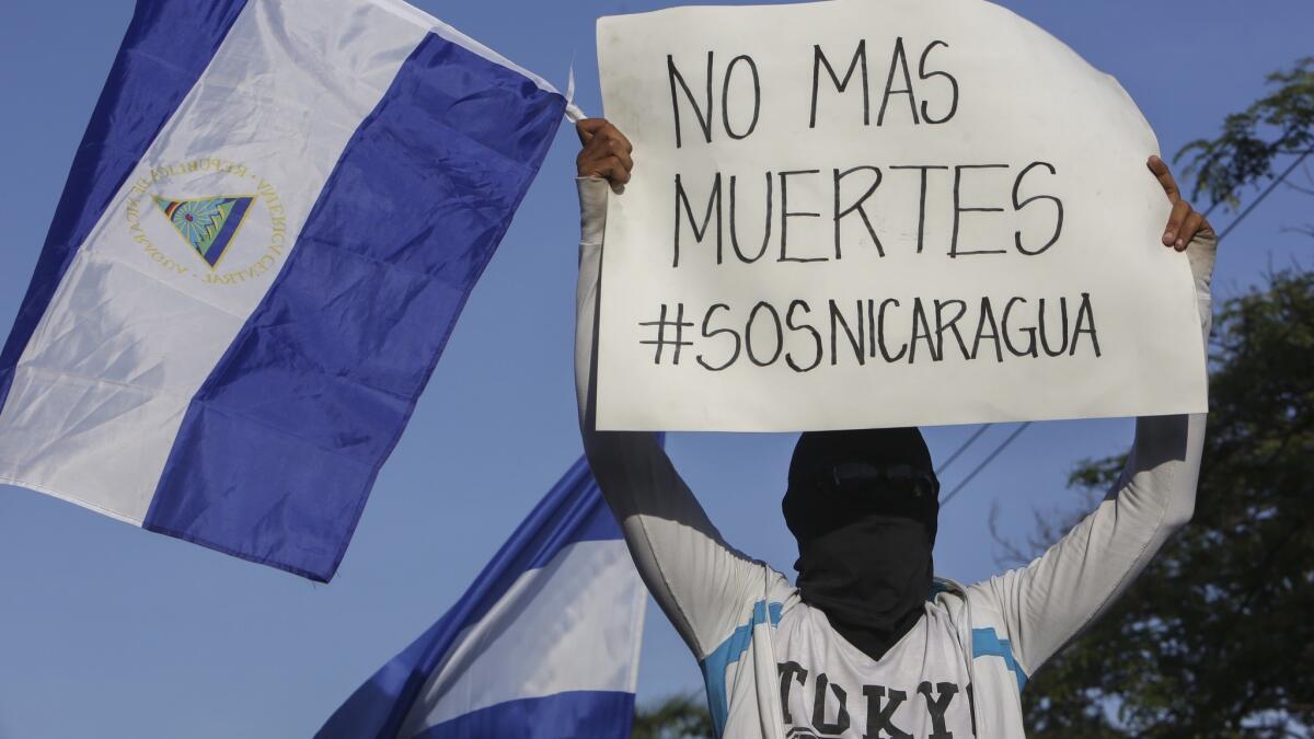 A masked demonstrator holding a Nicaraguan flag and a sign that reads in Spanish: "No more deaths," protests government repression in April 2018 in Managua.