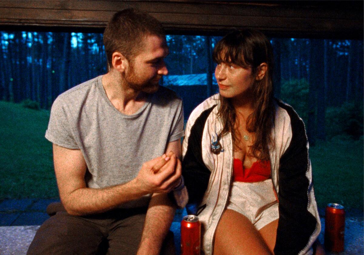 A young man and woman sit side by side in conversation in a scene from the film "Slow." 