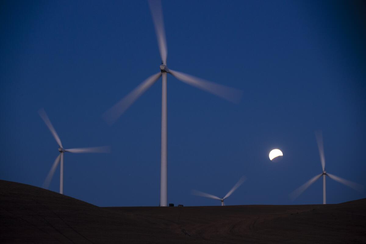 Turbines spin as the blood moon lunar eclipse sets behind the Shiloh II wind farm in California's Montezuma Hills in 2021.