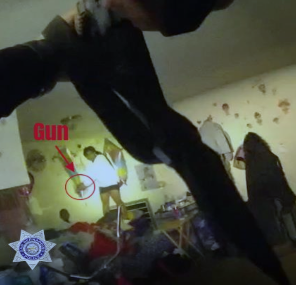 A still from video shows an officer's hands aiming a gun at a woman who is holding what's labeled as a gun.